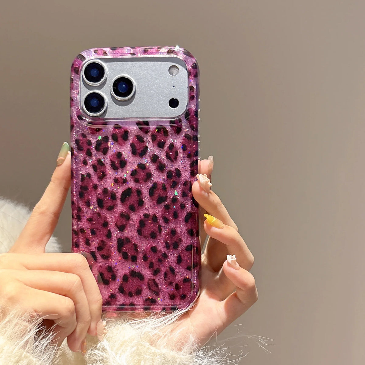 A hand holds a glamorous leopard print sequin shockproof phone case for an iPhone against a neutral background.