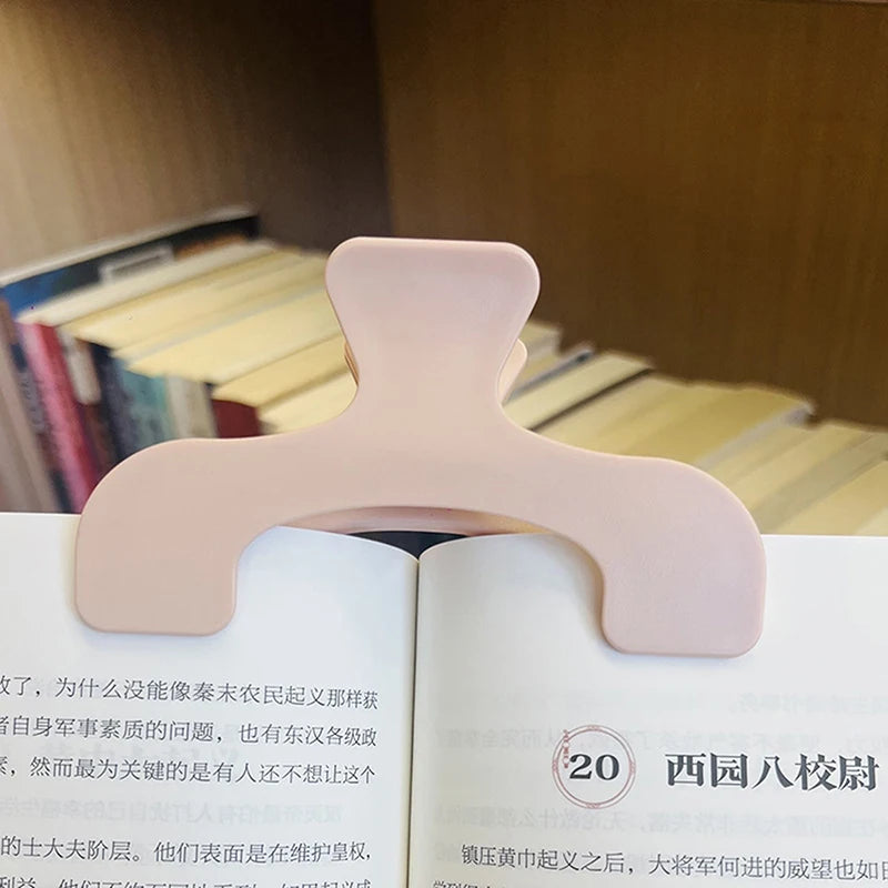 A close-up of pink book page clips with a rounded, ergonomic design resting on the edge of an open book.