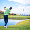 A man in a green shirt is swinging a golf club while a magnetic monopod records the shot.