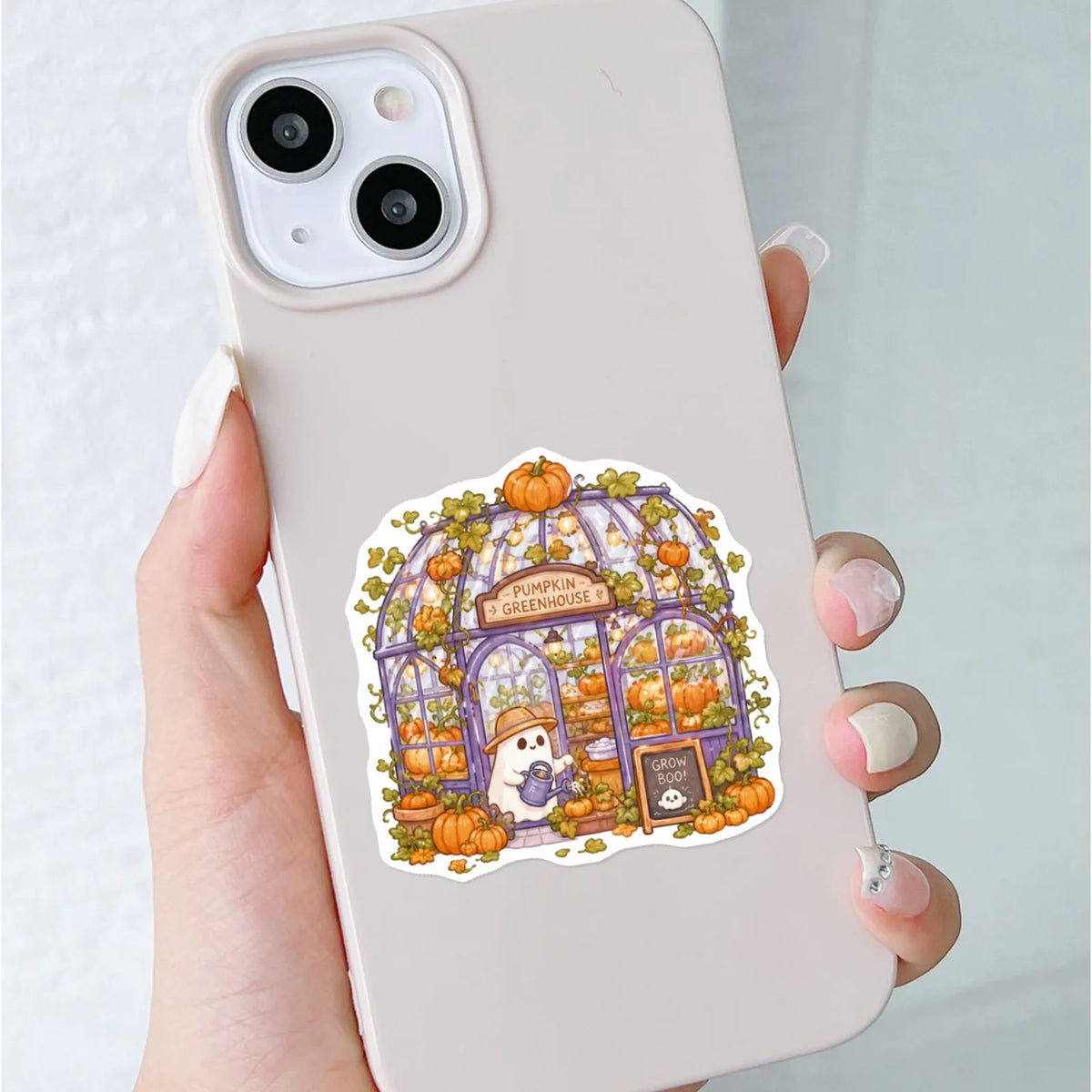A hand holds a phone displaying a pastel Halloween sticker pack featuring cute ghost, pumpkin, and dessert vinyl decals.