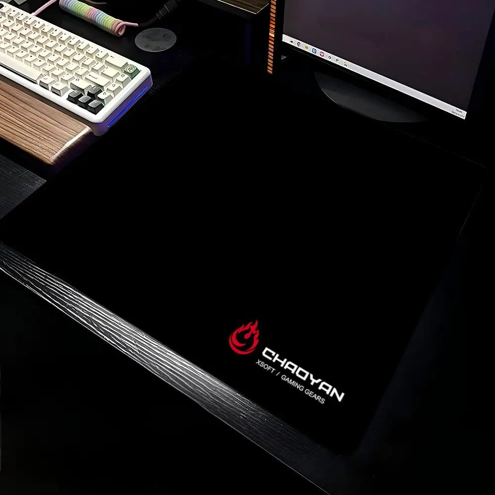 A black aesthetic gaming mouse pad is shown with a keyboard and a laptop in the background.