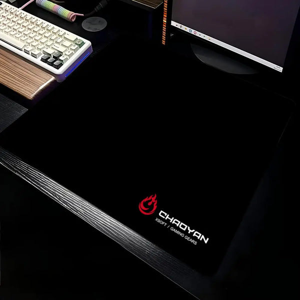 A black aesthetic gaming mouse pad is shown with a keyboard and a laptop in the background.
