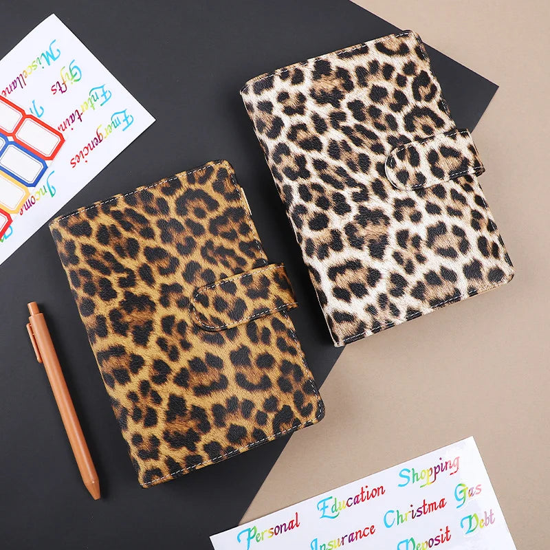 A leopard print A6 binder with a 6-hole loose leaf system resting on a dark surface.