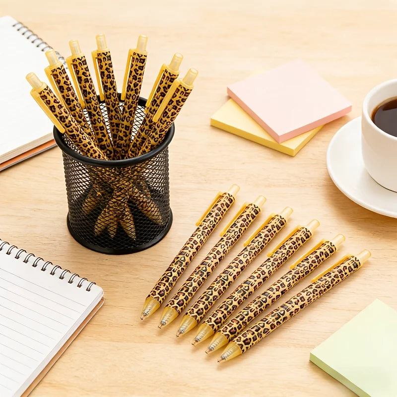 A collection of leopard print retractable ballpoint pens in black ink arranged on a wooden surface with notebooks.