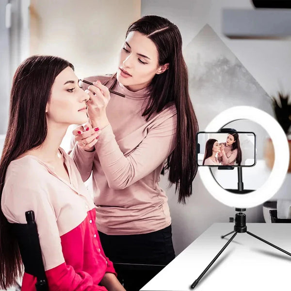 A woman is using an LED ring light with a tripod stand for makeup or streaming on her face.
