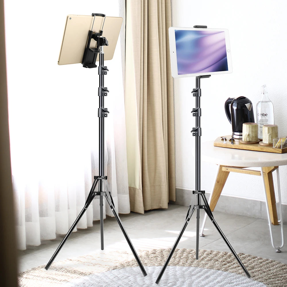 A black adjustable tripod mount is shown with a tablet attached, next to another similar mount and a wooden table.