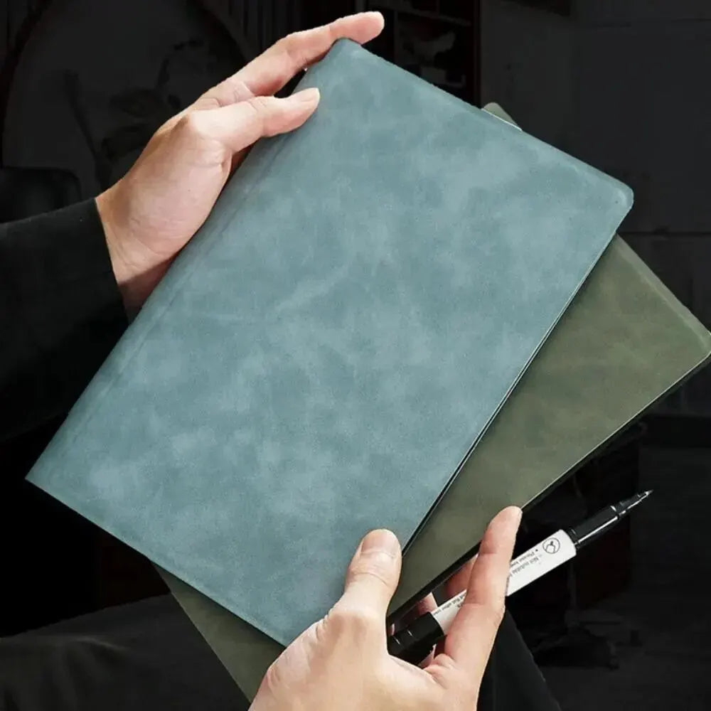 A hand holds a square, light blue reusable dry erase whiteboard with a dark green mat.