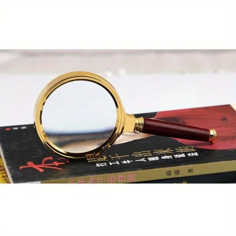 A gold-rimmed magnifying glass with a dark wooden handle resting on a book.