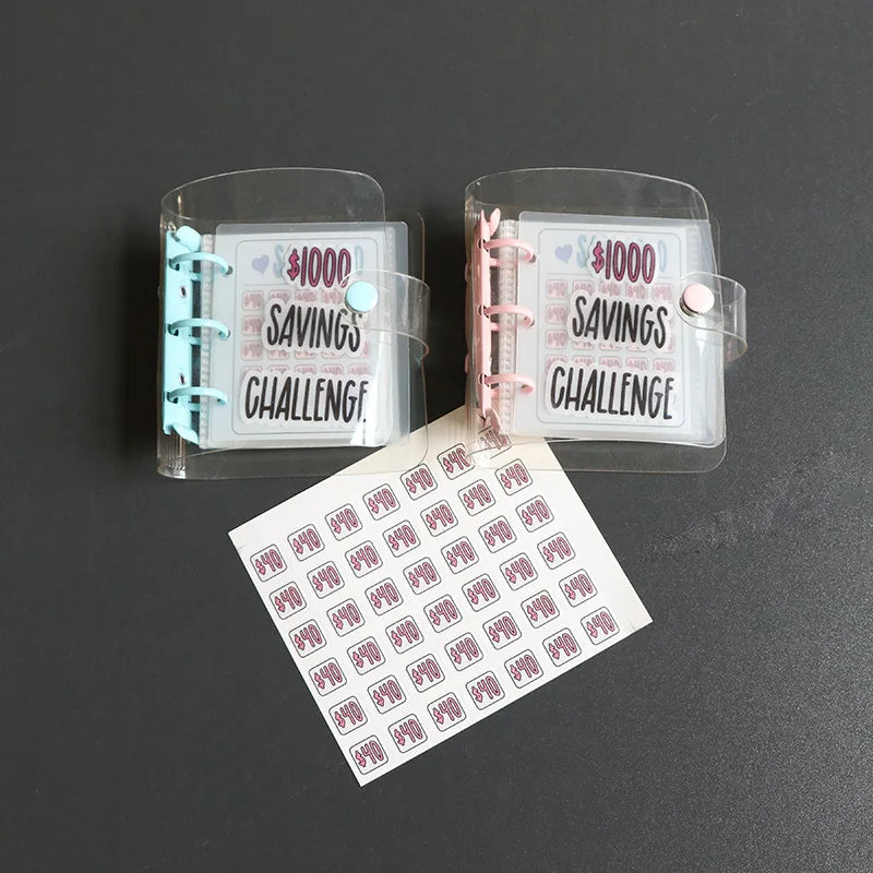 Two clear plastic binders labeled $1000 Savings Challenge, with a white sheet detailing the challenge.