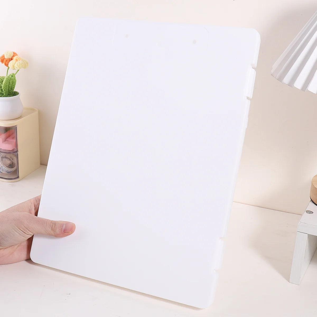 A white A4 document and photo storage file box being held by a hand on a light surface.