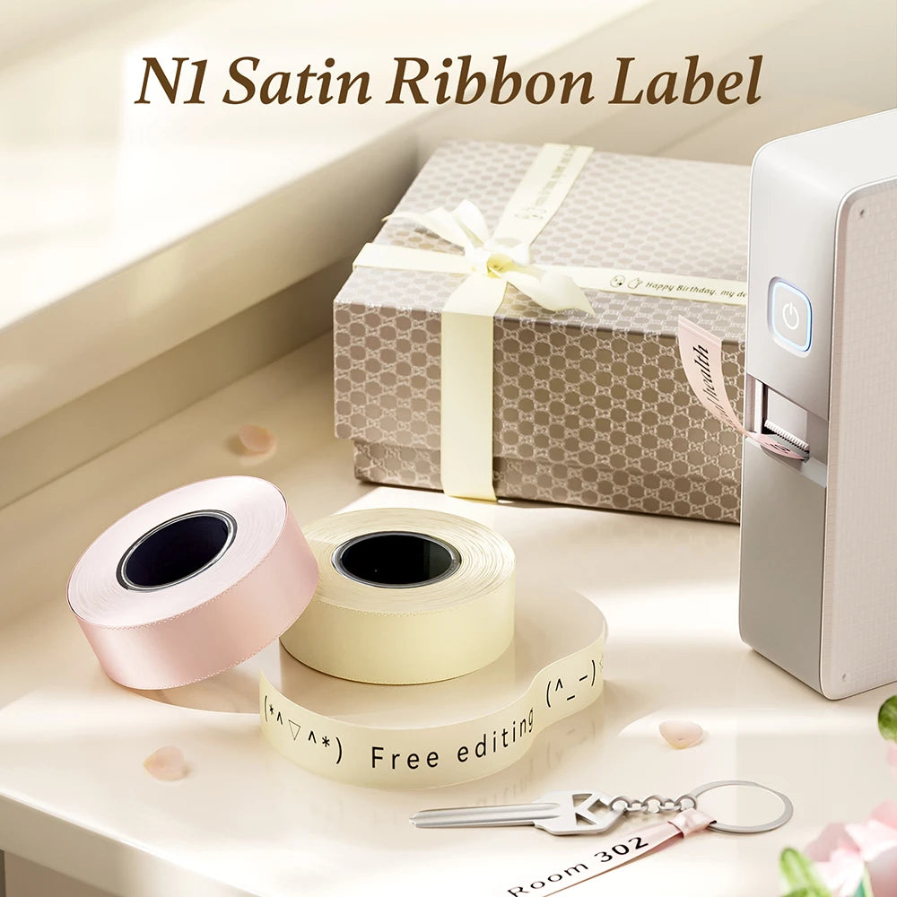 Un rouleau d'étiquette de ruban satiné rose et un rouleau d'étiquettes de ruban satiné crème à côté d'une imprimante et d'une
