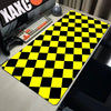 A yellow and black checkered desk mat is placed on a wooden desk next to a keyboard and gaming controller.