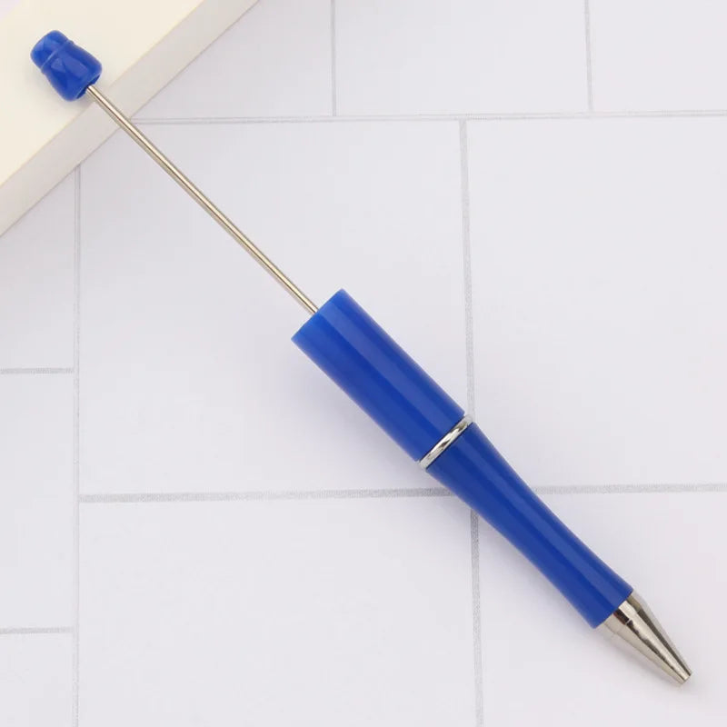 A blue DIY beadable pen with a silver tip resting on a white tiled surface.