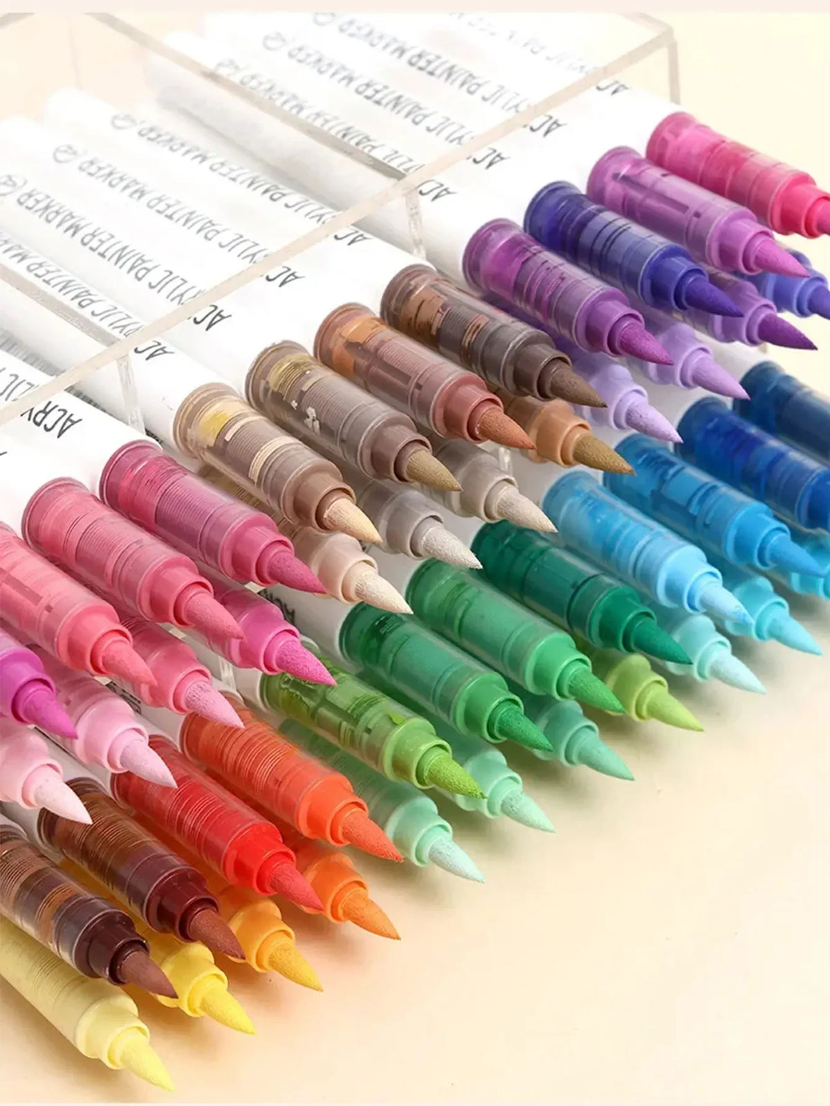 A collection of soft acrylic paint markers in various shades of pink, purple, blue, and green arranged on a white background.