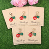 Five sets of cute ladybug and daisy keychains are displayed on pink cards on green grass.