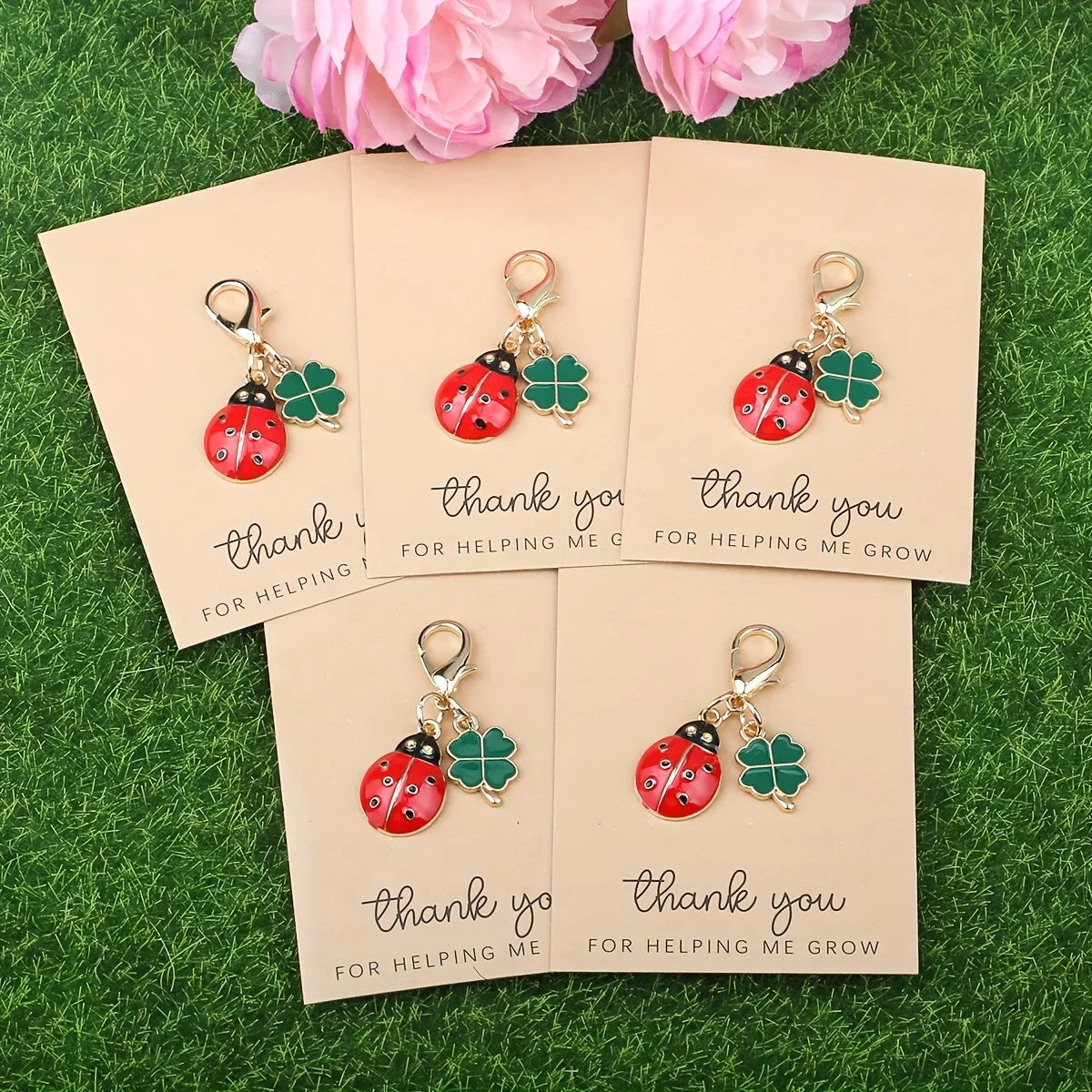 Five sets of cute ladybug and daisy keychains are displayed on pink cards on green grass.