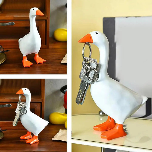A white resin duck key holder with orange feet is displayed on a wooden desk organizer.