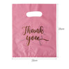A pink paper gift bag with a handle, featuring the text Thank you written in gold script.