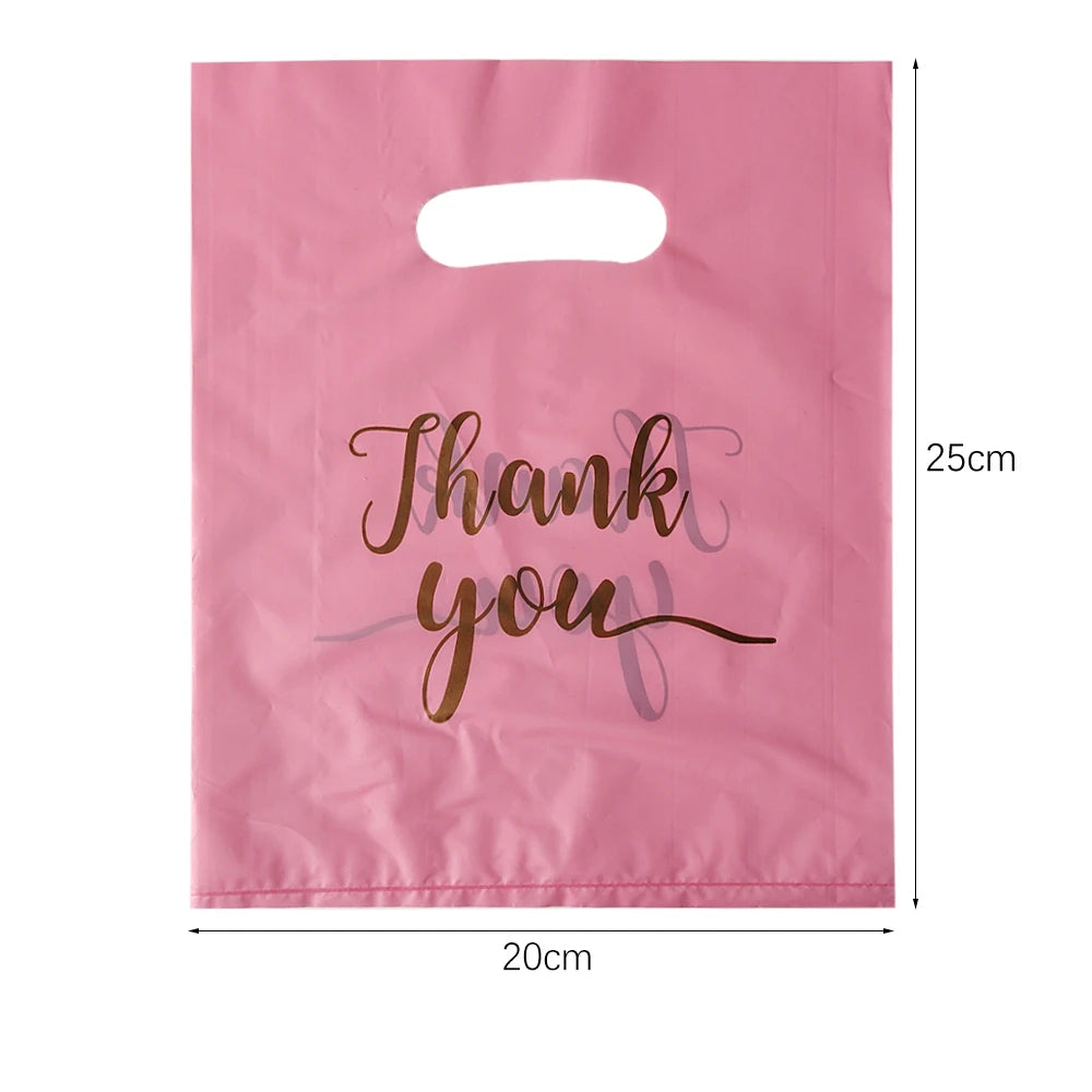 A pink paper gift bag with a handle, featuring the text Thank you written in gold script.