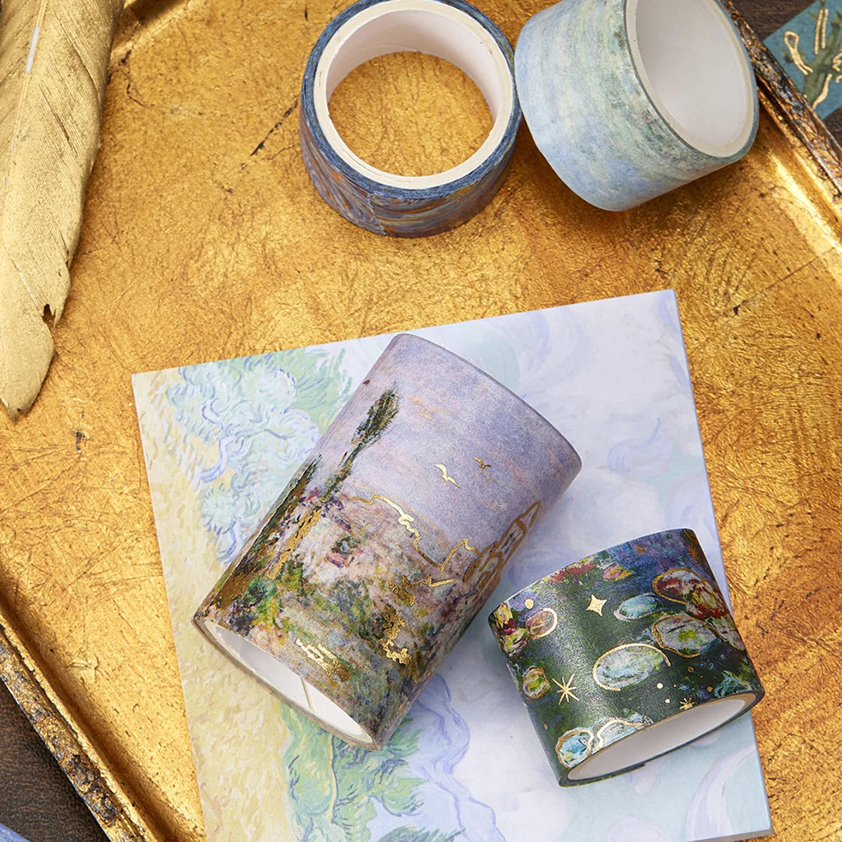 A set of oil painting themed decorative washi tape rolls resting on a gold tray and a piece of paper.