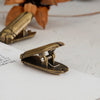 A set of antique brass metal beetle binder clips resting on a white surface.