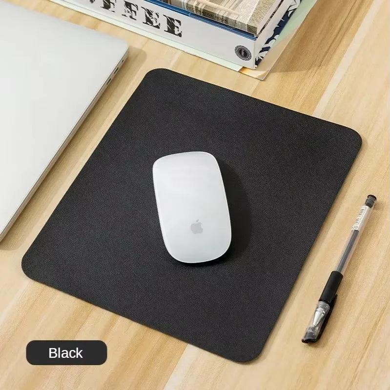 A black mouse pad with a stitched edge is shown on a wooden surface next to a white Apple mouse and a pen.