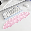 A pink, translucent bubble wrist rest is placed next to a white keyboard and a computer mouse on a desk.