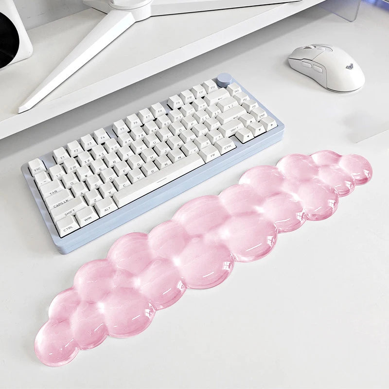 A pink, translucent bubble wrist rest is placed next to a white keyboard and a computer mouse on a desk.