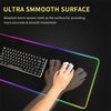 A hand is using a black keyboard and white mouse on an ultra smooth surface with glowing RGB lighting.