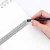 A hand holds a black pen against a stainless steel measuring ruler on a white notepad.