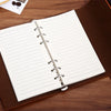 Cuaderno de cuero marrón encuadernado con espiral plateada y papel rayado sobre una superficie de madera.