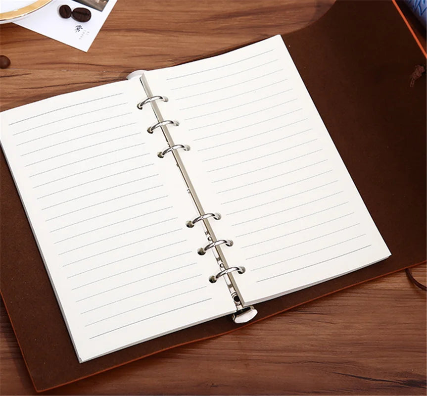 Cuaderno de cuero marrón encuadernado con espiral plateada y papel rayado sobre una superficie de madera.