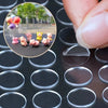 A close-up shot of small pink and purple adhesive dots arranged on a dark surface, with a hand holding a clear plastic piece.