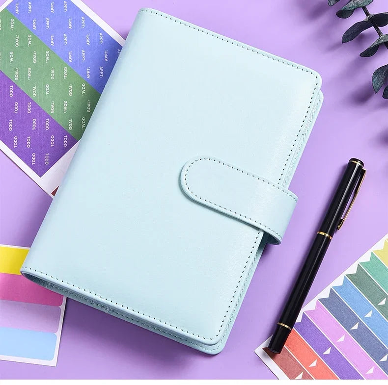 A light blue A6 budget planner with a leather cover and envelope system placed on a purple background.