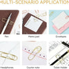 A collection of elegant metal pen clips, envelopes, a memo pad, headphones, and a ticket holder displayed on a wooden surface