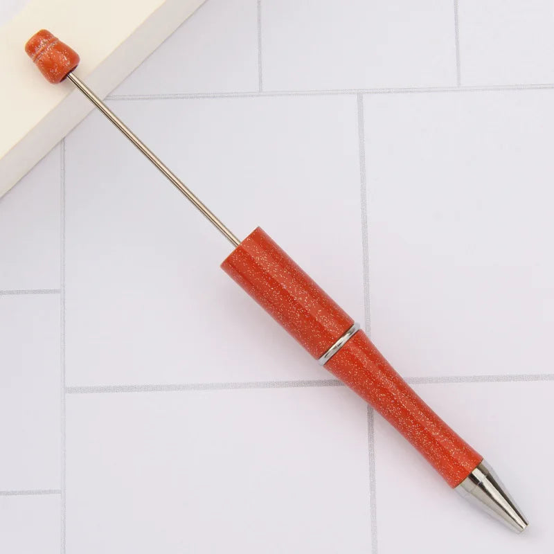 A DIY beadable pen set with an orange-red body and silver tip is shown on a white surface.