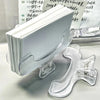 A clear plastic clip holds a stack of white book page clips on a white surface.