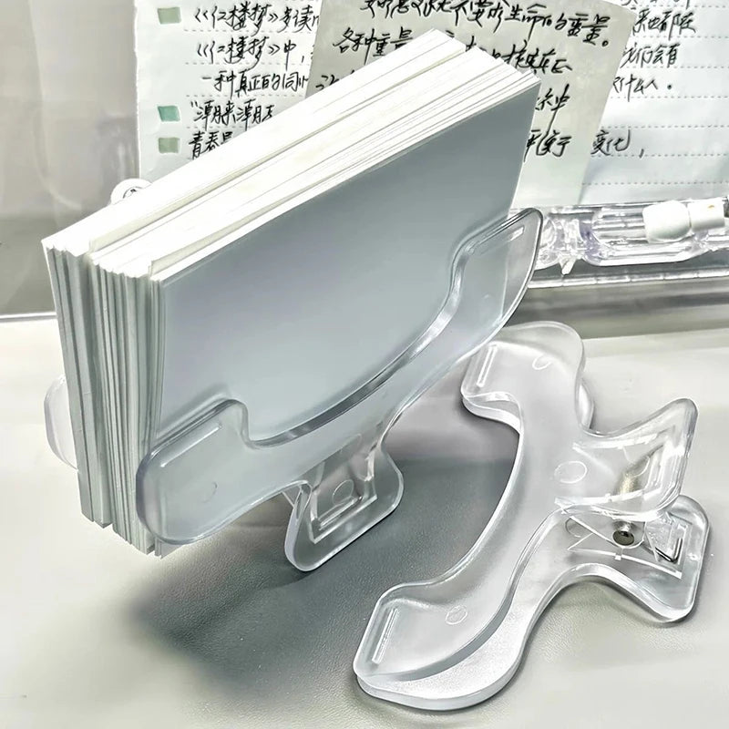 A clear plastic clip holds a stack of white book page clips on a white surface.