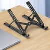 A black portable folding laptop stand is shown resting on a wooden surface next to a silver laptop.