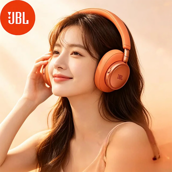 Une femme portant des écouteurs JBL orange, souriante et touchant son oreille, dans une lumière douce.