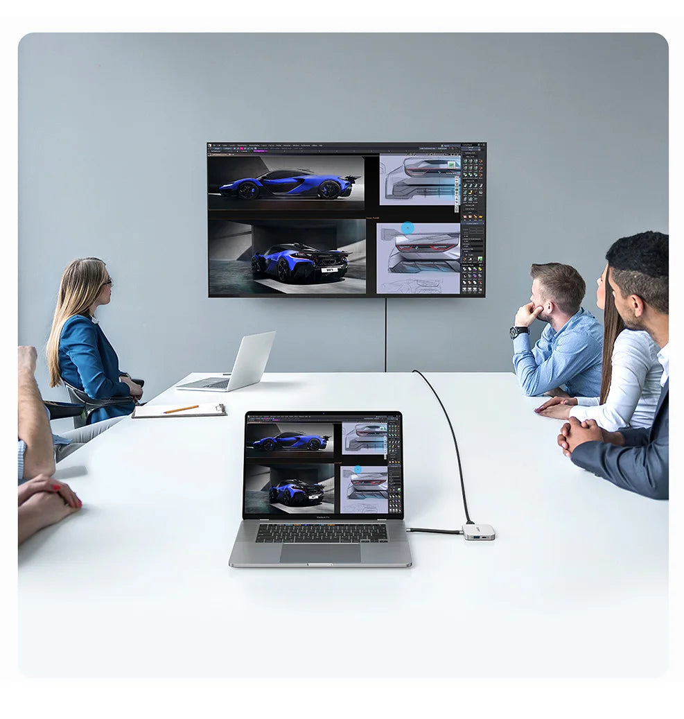 Three professionals collaborate around a table with a large monitor displaying car models and laptops.
