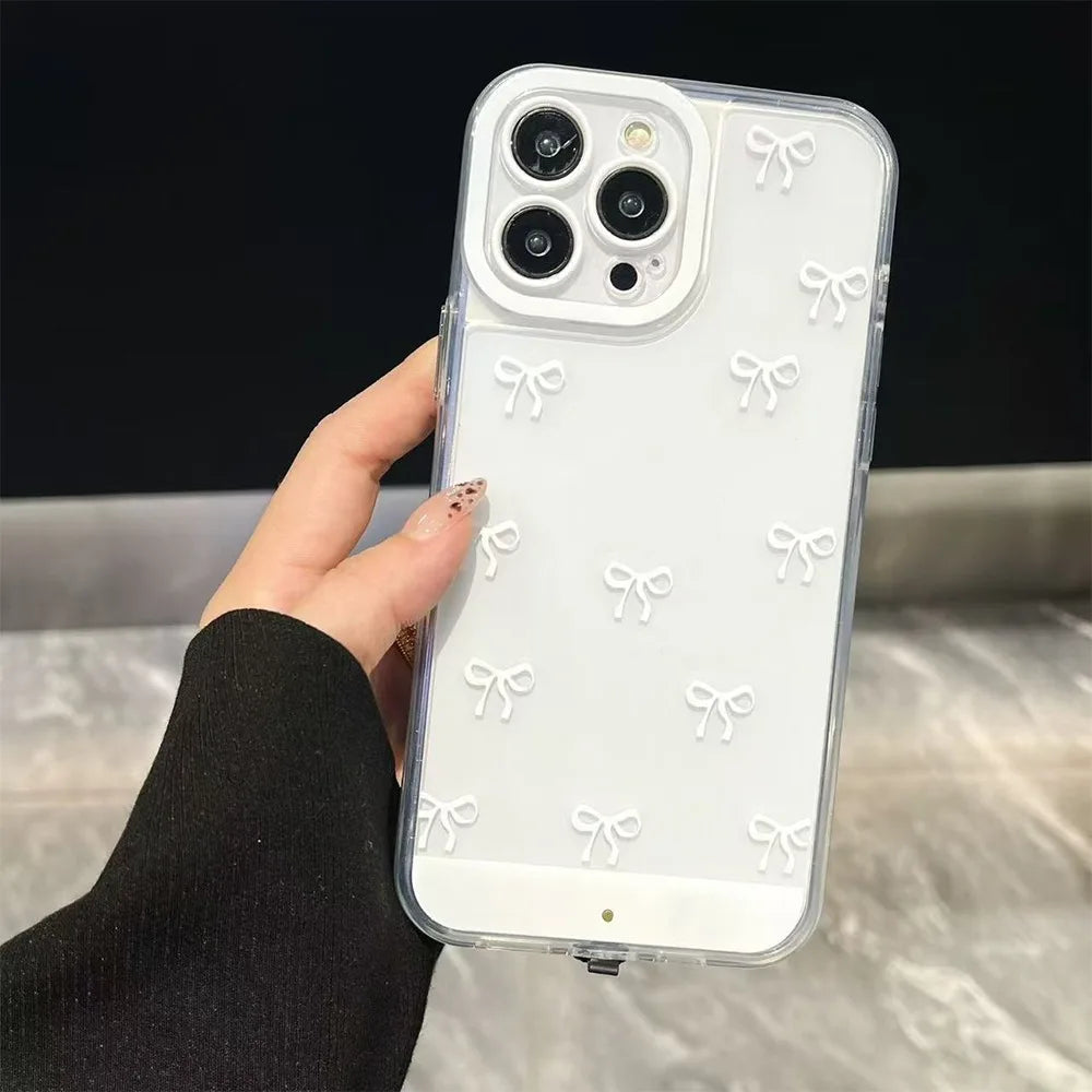 A clear silicone case with white bowknot decorations is shown on an iPhone, held by a hand.