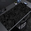 Extra large abstract desk mat with black and white wavy lines on a dark surface.