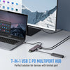 A silver laptop is connected to a 7-in-1 USB-C multiport hub on a desk with a monitor in the background.