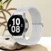 A silver nylon watch strap is shown coiled around a smartwatch, resting on a light-colored stone.