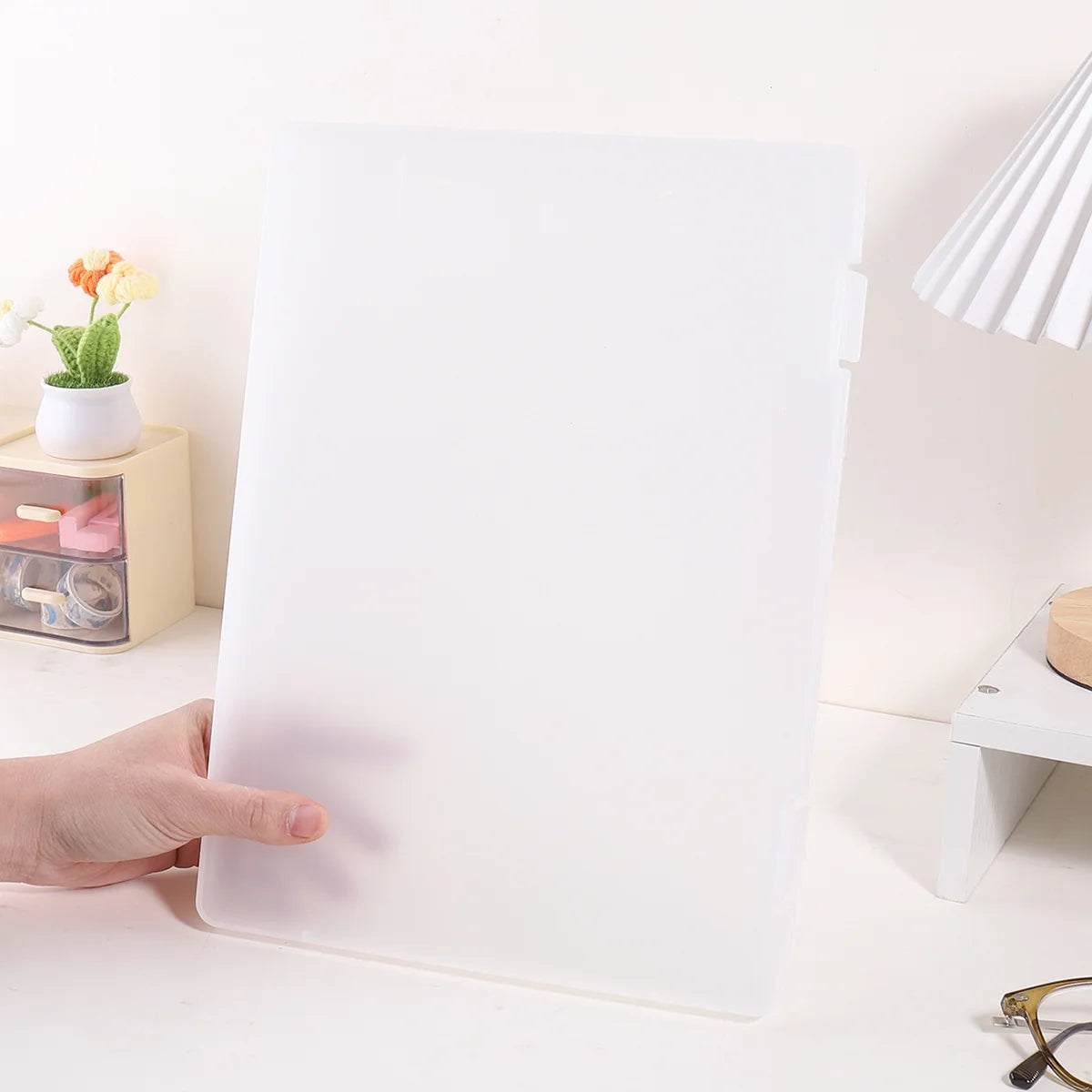 A white A4 document and photo storage file box is being held by a hand on a white surface.