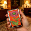 A hand holds a vintage stainless steel card and cash case featuring a pink flower design on an orange background.
