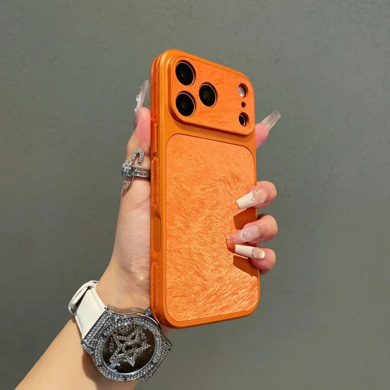 An orange phone case with a frosted velvet texture is held by a hand wearing a silver bracelet.