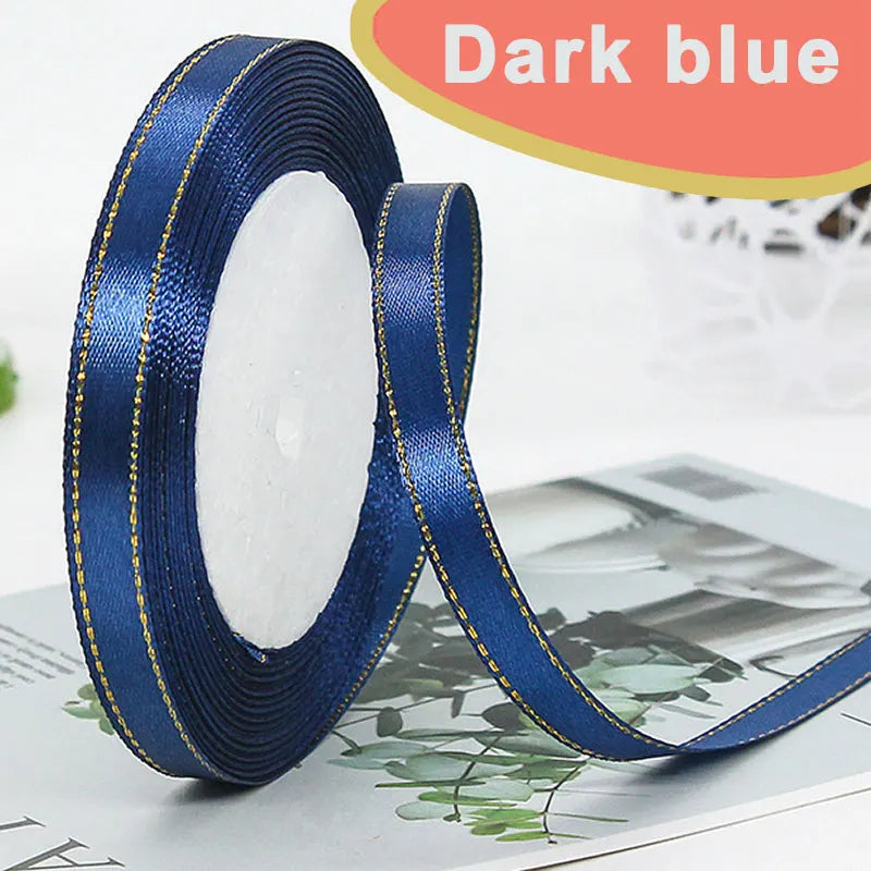 Roll of dark blue satin ribbon with gold edge and a white center, displayed on a surface.