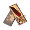 A wooden box containing a dip pen set with a leather-colored feather, several nibs, and an antique-style compass.